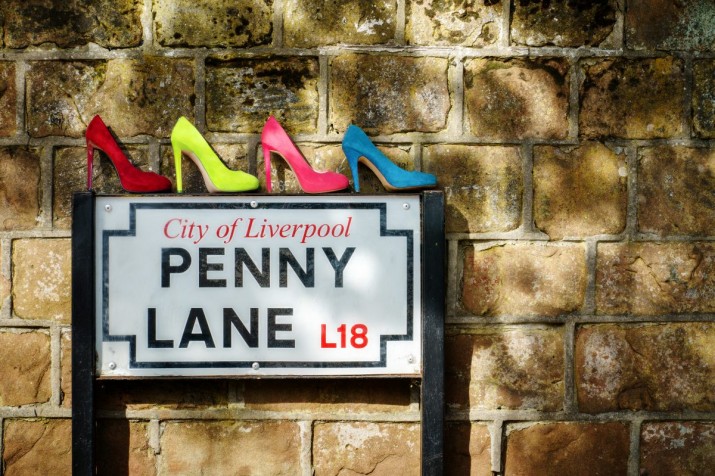 four pairs of ladies shoes, in colours of Sergeant Pepper, atop of the Penny Lane street sign in Liverpool